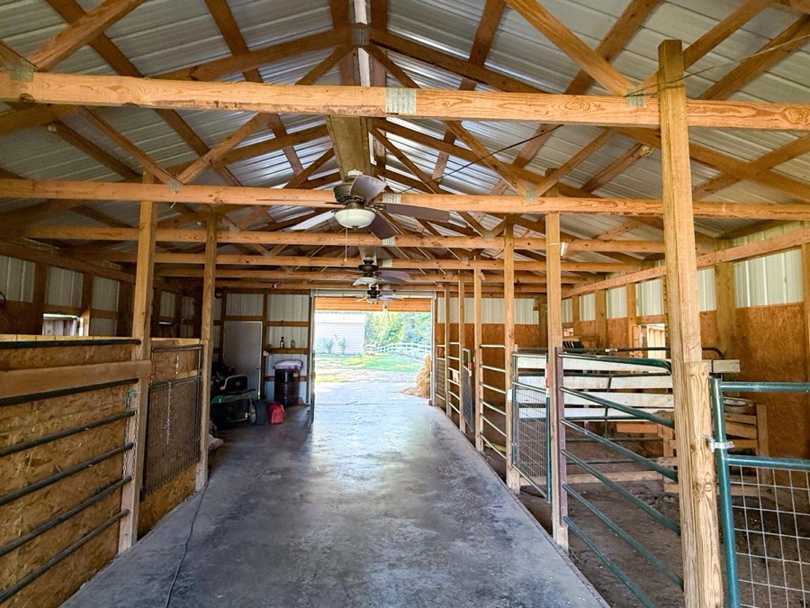 Inspira Ranch horse stables interior with wooden beam construction and open grounds beyond