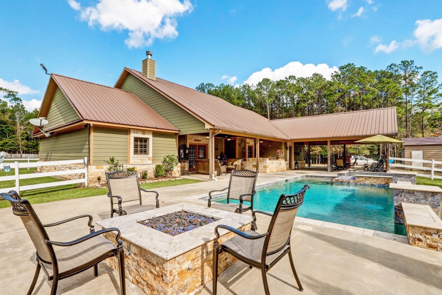 Inspira Ranch main house exterior with inground pool, stone fire pit seating, and blue sky